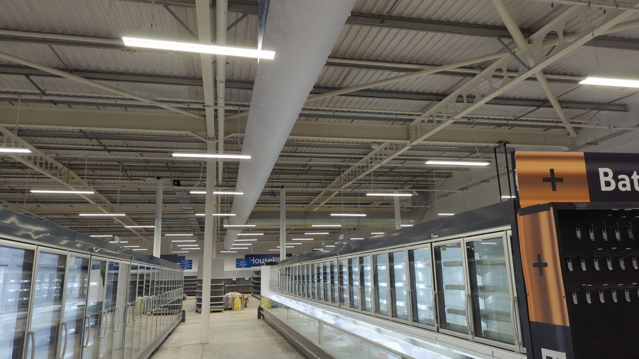 Interior of the converted Tesco store showing freezer aisles, suspended lighting and brand signage